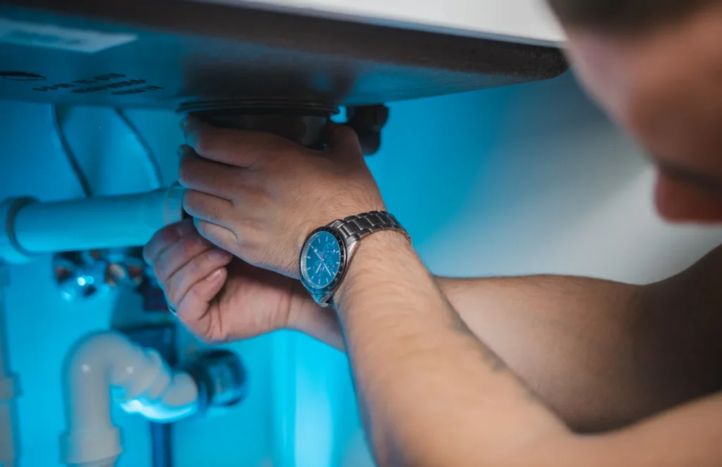 Plumber tightening a drain pipe connection under a sink
